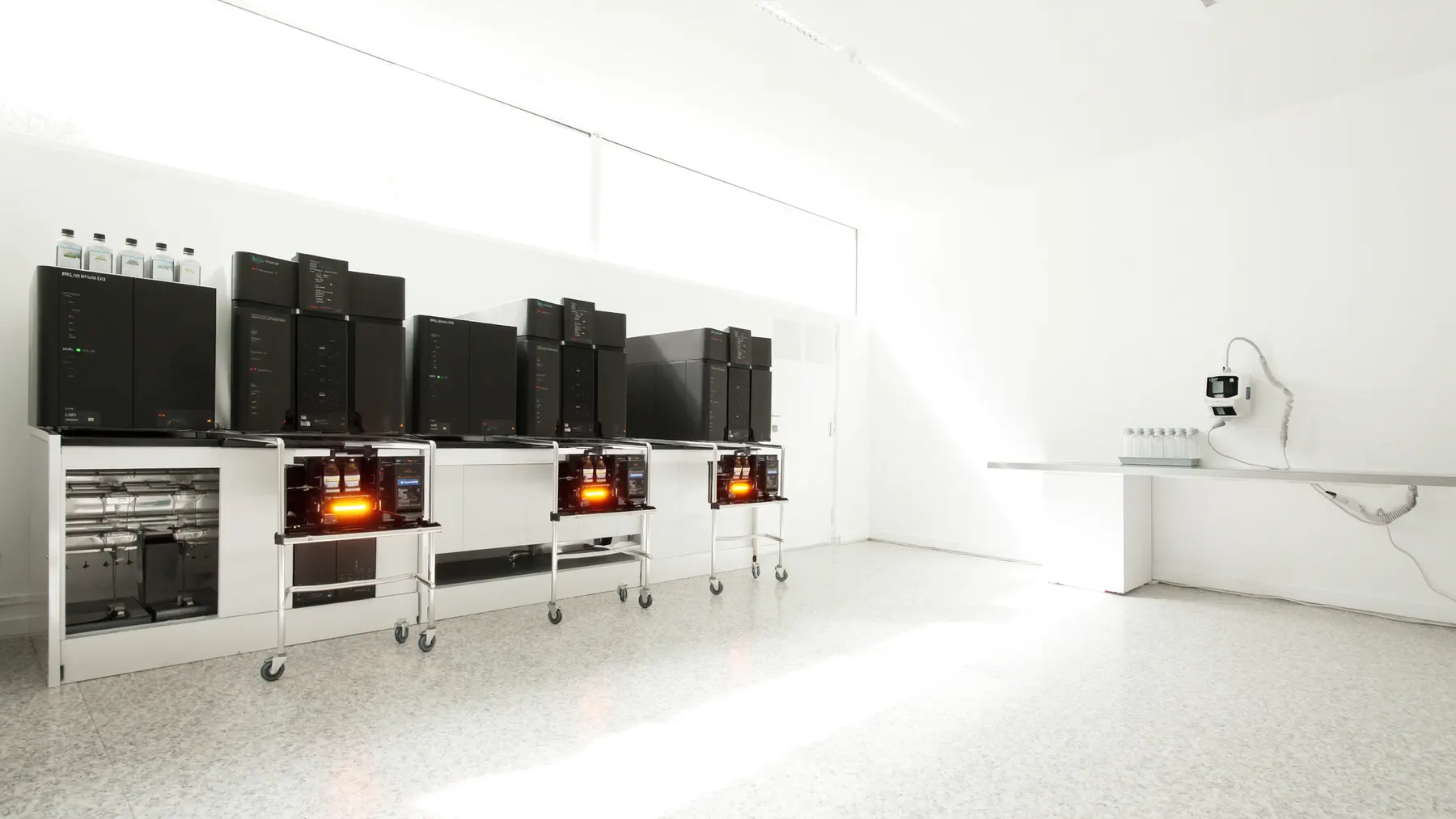 A bright analytical chemistry laboratory with a row of chromatography instruments and racked glass vials.